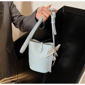 Détail d'un sac seau en cuir bleu clair à motif litchi avec breloque papillon perlé