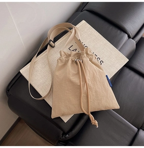 Detail view of beige nylon drawstring bucket bag with adjustable strap and blue woven label