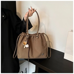 Detail of khaki drawstring tote bag with baseball charm and metallic logo badge