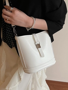 Sac seau minimaliste en cuir blanc avec boucle métallique porté en bandoulière élégante