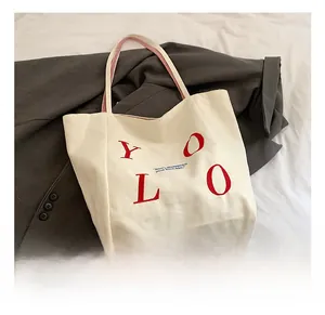 Detail of canvas tote bag with bold red YOLO text and striped red and white woven handle