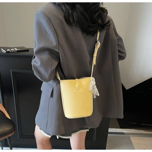 Détail d'un sac seau jaune à motif litchi avec breloque en perles porté par un mannequin