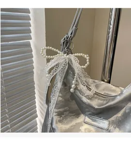 Detail of silver tote bag featuring a white lace bow and elegant pearl charms decorations