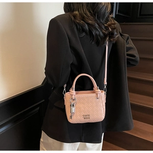 Close-up of pink woven bucket bag with metallic logo and silver lock charm on model