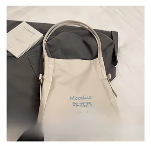 Close-up of cream tote bag featuring blue Mooduo lettering and side ribbon detail