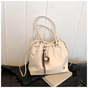 Detail of a beige drawstring tote bag with smooth texture and baseball charm on a leather jacket