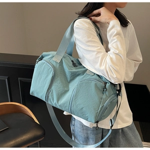 Blue nylon travel bag with shoe compartment shown on a model in a modern interior