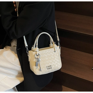 Detailed view of cream woven bucket bag texture with silver key charm and shoulder strap