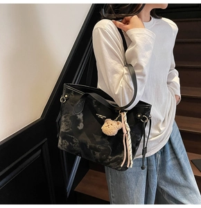 Detail showing marble-patterned black tote bag with plush bear and tassel charm accessories