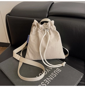 Detail view of cream nylon drawstring bag with blue label on dark leather background