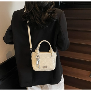 Detail of cream woven bucket bag showing metal COIN 2DN logo and key charm on strap