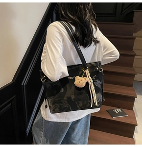 Woman carrying a black glossy leather tote bag with bear charm on wooden stairs