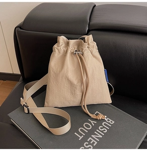 Detail view of a beige drawstring nylon bucket bag with a small blue logo on a leather sofa