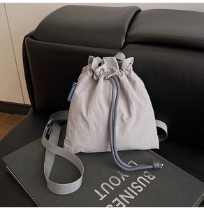 Close-up of gray nylon drawstring bucket bag with silver metal cord lock and blue brand tag