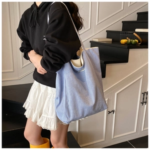 Detailed shot of large blue and white striped canvas tote bag worn by a model