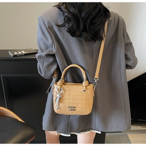 Detail of woven texture bucket bag in brown with metal key pendant and logo