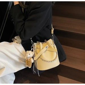 Detail der beigen Bucket Bag mit Litschimuster und Bärenanhänger an einem Model