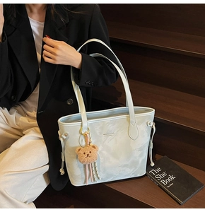 Close-up of light blue faux leather tote bag with stylish bear charm on wooden stairs