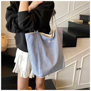 Blue and white striped canvas tote bag with decorative label shown on shoulder of a model