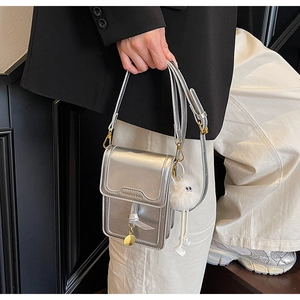 Detail showing metallic silver mini phone bag with plush doll charm and gold hardware