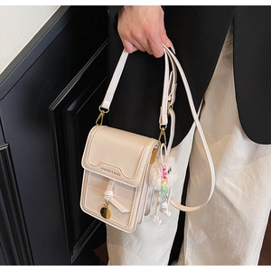 Detail of cream crossbody phone bag with gold charm and white plush toy pendant accessory