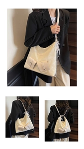 Detail of cream versatile tote bag showing multi-way straps and lace pearl charm accessory