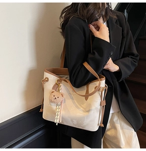 Close-up of a cream and brown tote bag featuring a cute plush bear charm and tassel detail