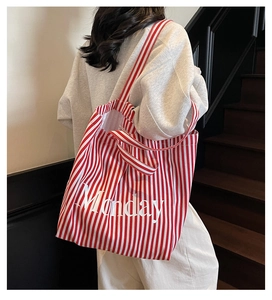 Detail of red and white striped canvas tote bag with Monday print worn on shoulder