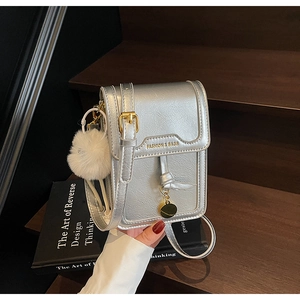 Detail of silver textured leather phone bag with gold hardware and white plush keychain