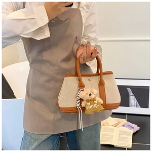 Detail of canvas and brown leather stitching on a mini tote bag with cute bear charm