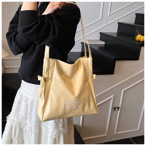 Detail of soft yellow tote bag with ribbon bows and embroidery on a model