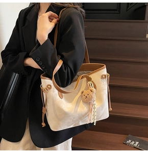 Detail of a large cream and brown leather tote bag with a cute plush bear charm
