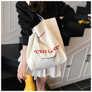Detail of white canvas tote bag with red C'EST LA VIE embroidery and blue text accents