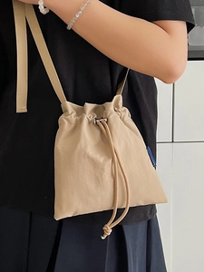 Minimalist beige nylon drawstring crossbody phone bag worn by a model on white background