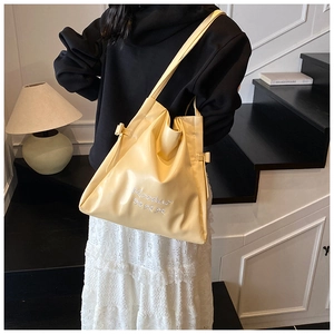 Detail of soft pale yellow PU leather tote bag with embroidered logo and bow decoration