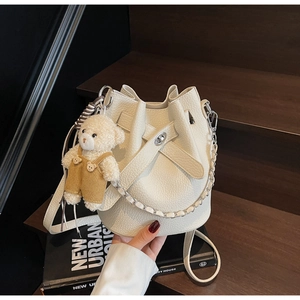 Detail einer weißen Eimer-Tasche mit Lychee-Narbung, Silberkette und kleinem Bärenanhänger