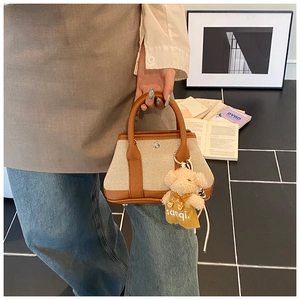 Detail of canvas bucket bag with brown leather trim and a cute plush bear charm