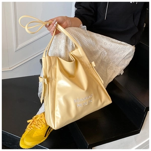 Detailed side view of yellow tote bag with bows and embroidery on dark stairs