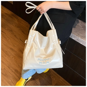 Close-up of the beige glossy PU leather tote bag featuring a blue Mooduo logo and bow detail