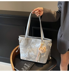 Detail of silver tote bag with crinkled texture and cute teddy bear charm pendant