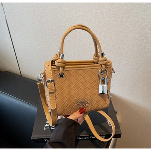 Detail of woven texture, round handle, and metal lock on this caramel bucket bag