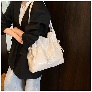 Detail view of cream white patent leather tote bag with Moduo embroidery and bow accents