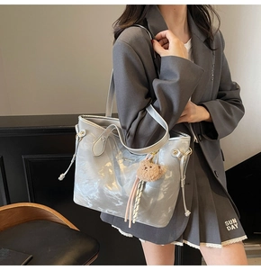 Side view of silver tote bag with plush bear charm and metallic glossy finish texture