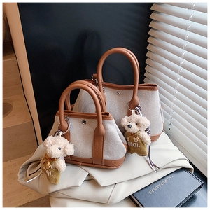 Detail of canvas bucket bag with brown leather trim and cute bear plush charm