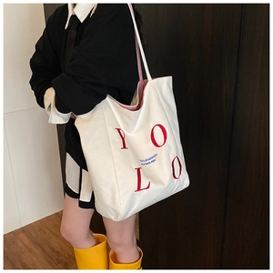 Canvas tote bag detail showing YOLO red embroidery and blue printed motivational slogan