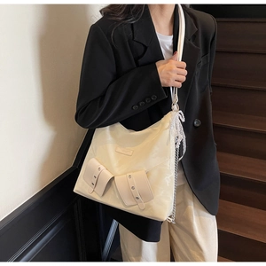 Close-up of off-white nylon tote bag with dual front pockets and pearl lace charm detail