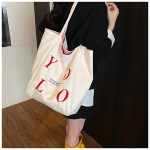 Detail view of large white canvas tote bag with red YOLO print and striped inner lining