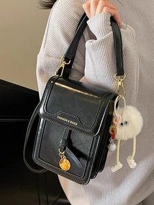 Fashionable black leather crossbody phone bag with gold charm and white plush toy