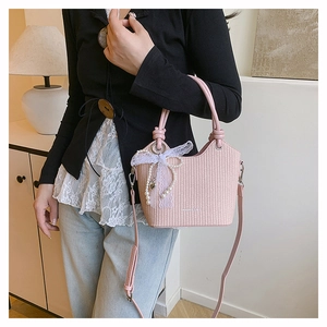 Détail du sac seau rose tressé avec des rubans en dentelle et des breloques en perles