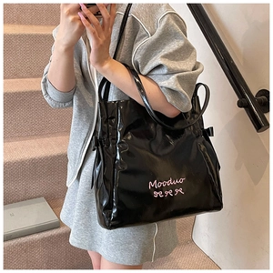 Detail of glossy black tote bag featuring pink Mooduo embroidery and side drawstring bows